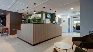 A reception area with a wooden reception desk, a TV, and a seating area with a round table and chairs. - Campanile NATURE - Vierzon (Vierzon)