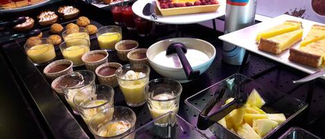 A buffet with various desserts and beverages, including custard, fruit, and pastries.