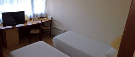 Una habitación con escritorio, computadora, dos camas, una silla y ventana con cortinas.