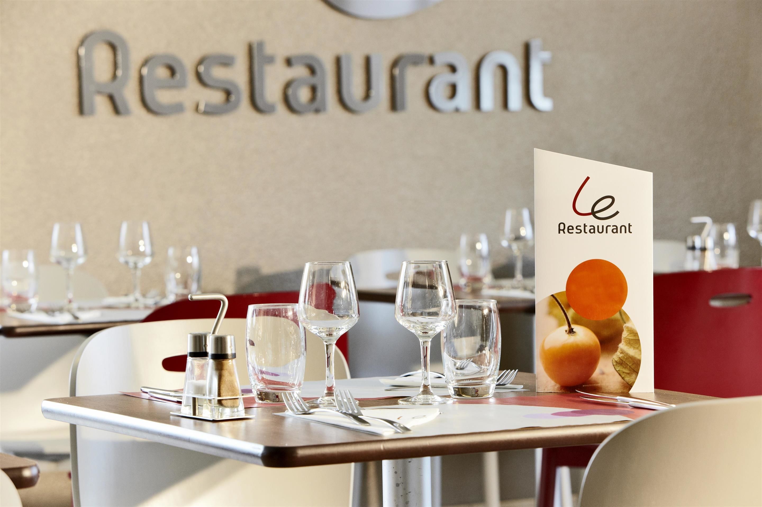 A restaurant interior with tables set for dining, a menu stand, and a wall sign reading "Restaurant".
