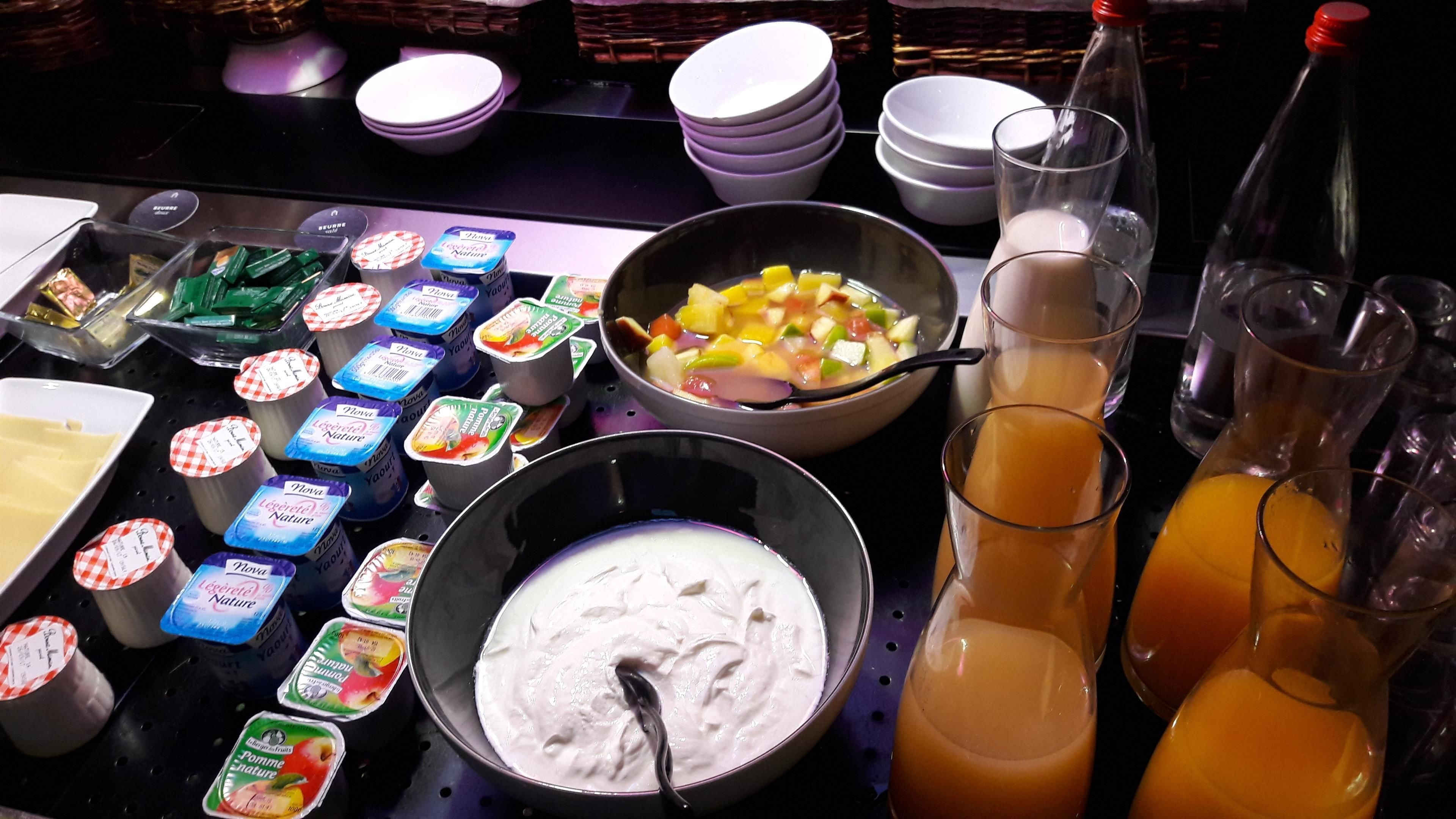 A buffet table with various food items, including yogurt, fruit salad, and juices.