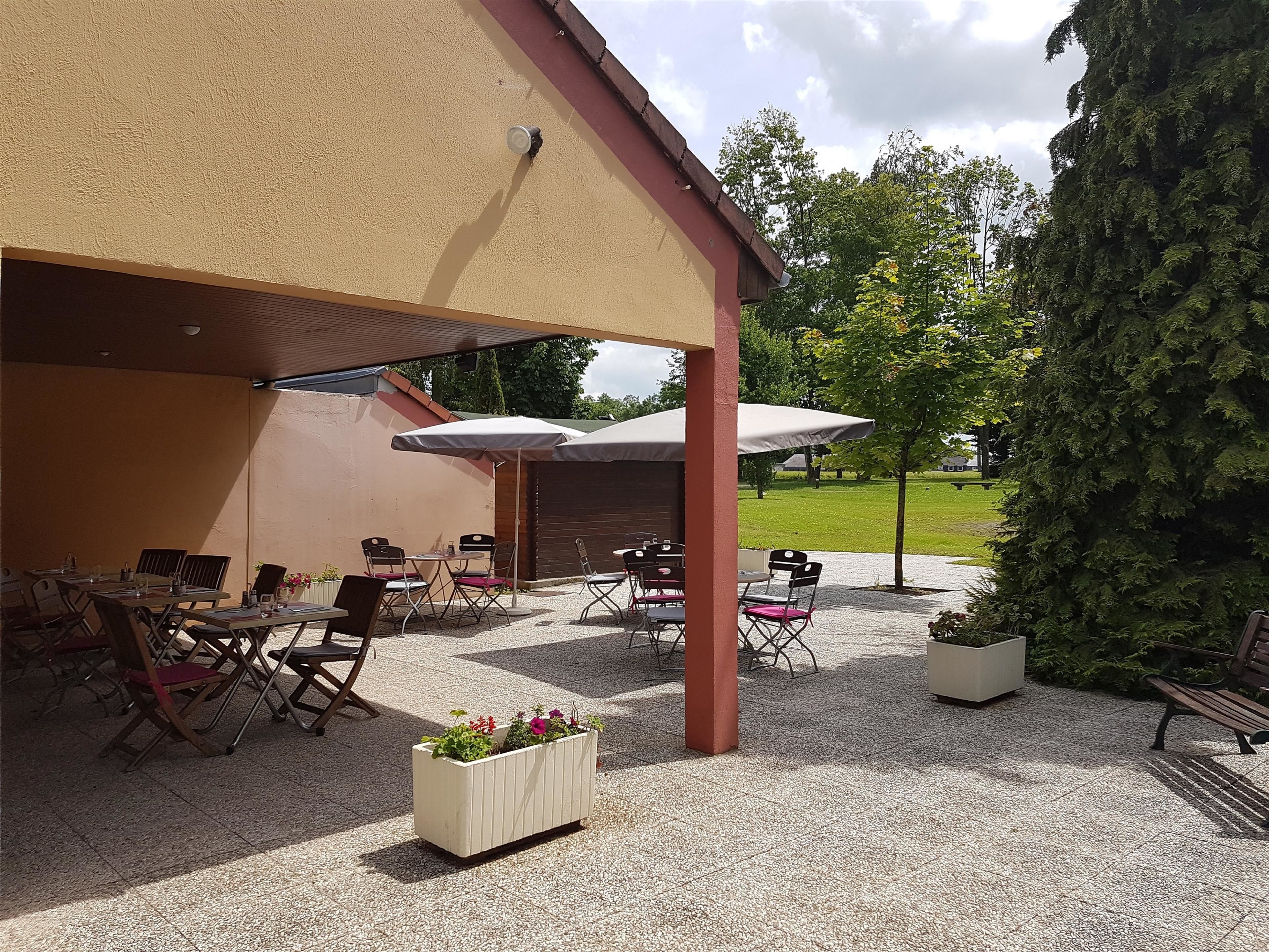 Una terrazza esterna con tavoli e sedie, un'area salotto coperta e un vaso fiorito.