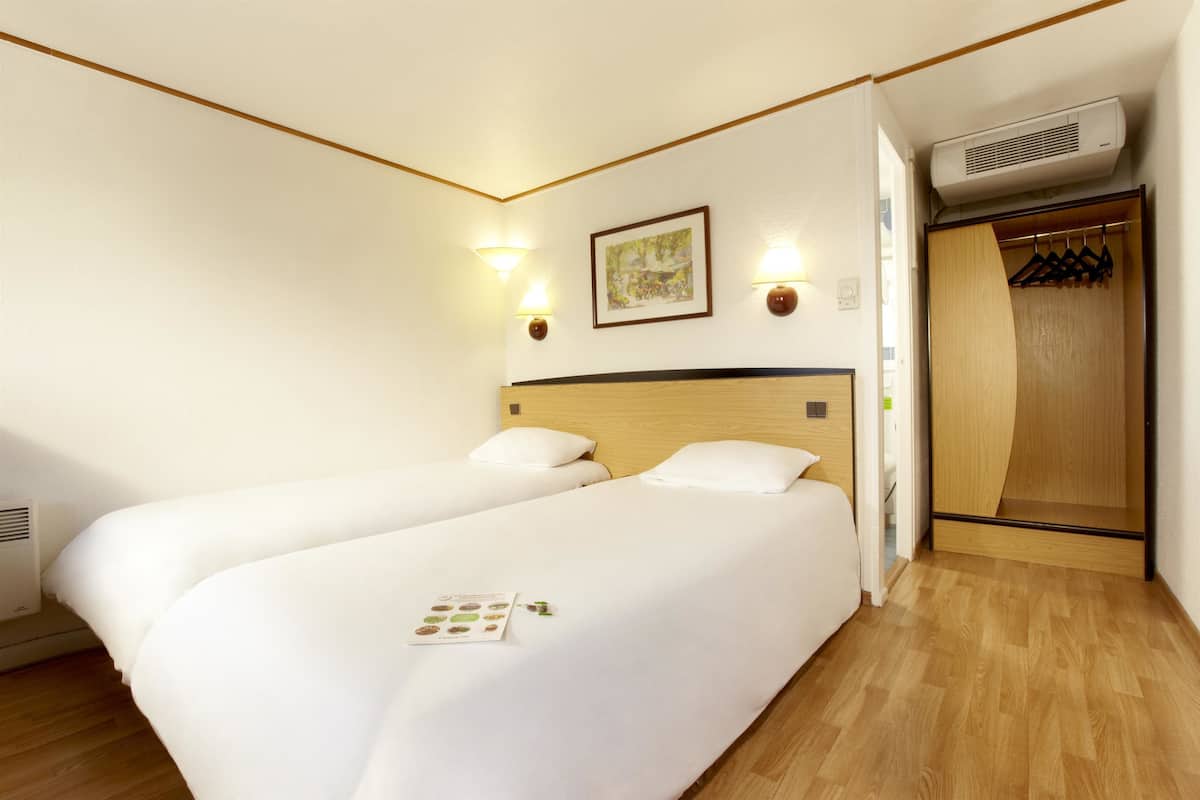 Habitación de hotel con dos camas, un armario de madera y aire acondicionado instalado en la pared.