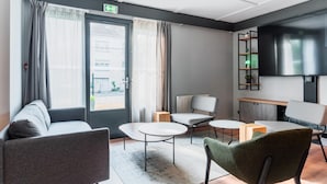A modern hotel room with a sofa, two armchairs, a small table, and a TV mounted on the wall. - Campanile NATURE - Thionville Yutz (Yutz)