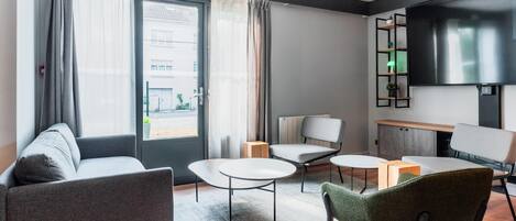 Una habitación de hotel moderna con sofá, dos sillones, una mesita y un televisor montado en la pared.
