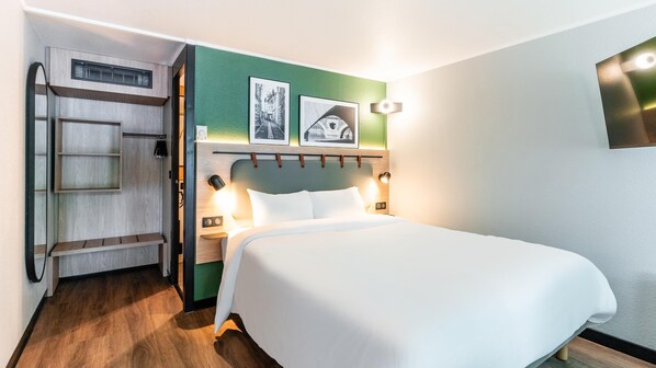 A hotel room with a bed, a wardrobe, a mirror, and two framed pictures on the wall.