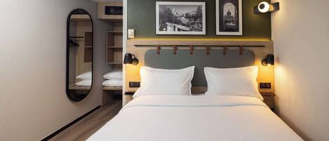Una habitación de hotel con una cama, dos lámparas de noche, un espejo y dos cuadros en la pared.