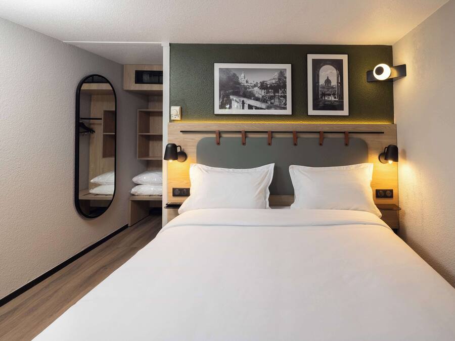 Una habitación de hotel con una cama, dos lámparas de noche, un espejo y dos cuadros en la pared.