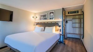 A hotel room with a large bed, a flat-screen TV mounted on the wall, and a wooden bench in the corner. - Campanile NATURE - Thionville Yutz (Yutz)
