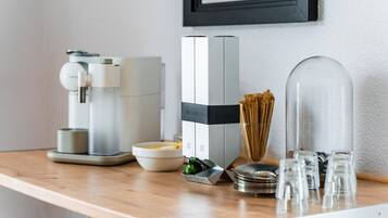 A coffee machine, a Nespresso coffee maker, a glass container with coffee pods, a bowl, and a clear glass pitcher on a wooden counter.