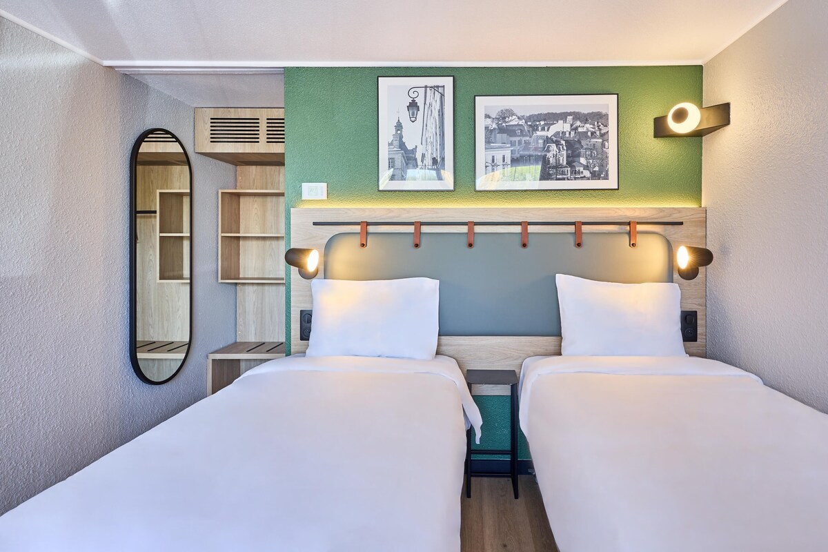 Ein Hotelzimmer mit zwei Betten, einer grünen Akzentwand und zwei gerahmten Bildern.