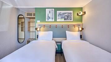 A hotel room with two beds, a green accent wall, and two framed pictures.