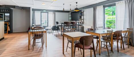 A modern dining area with wooden tables and chairs, a bar area, and large windows with curtains.