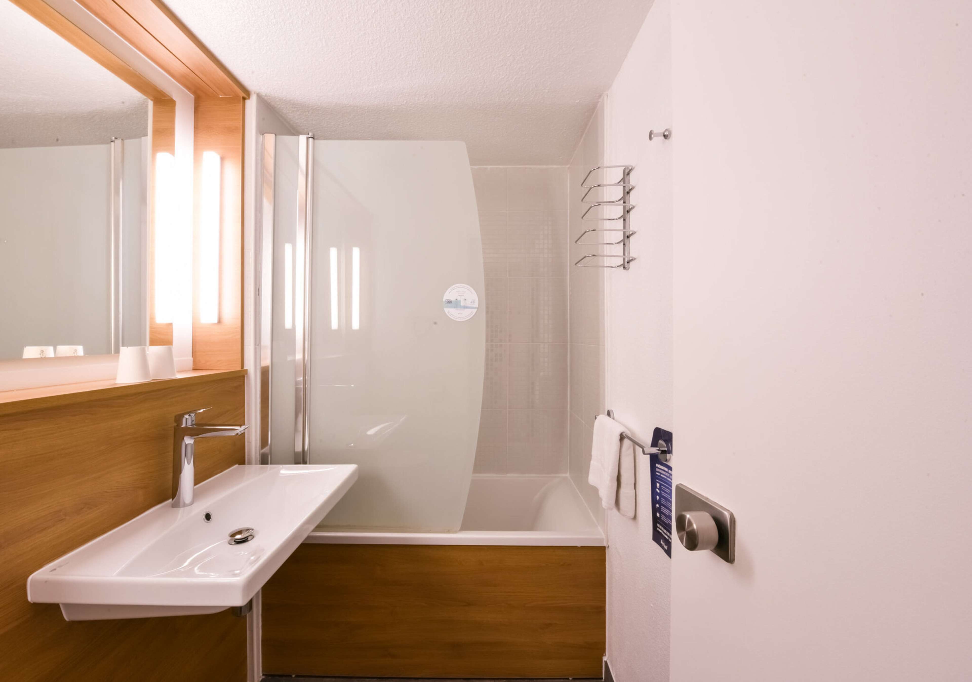 A modern bathroom with a sink, mirror, shower, and towel rack.