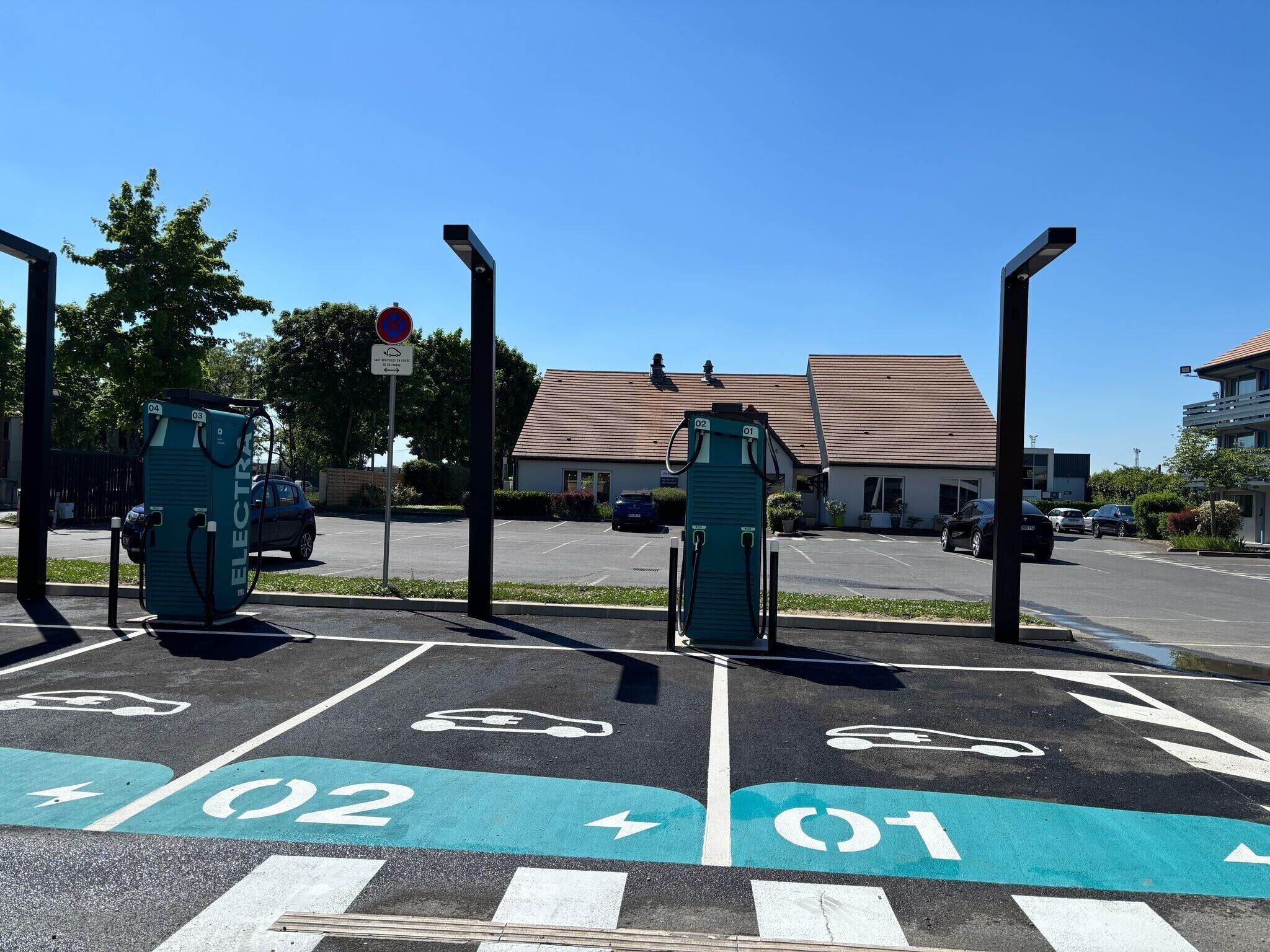 A parking area with electric vehicle charging stations, marked parking spaces, and a building in the background.