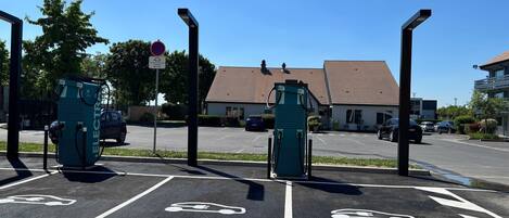 A parking area with electric vehicle charging stations, marked parking spaces, and a building in the background.