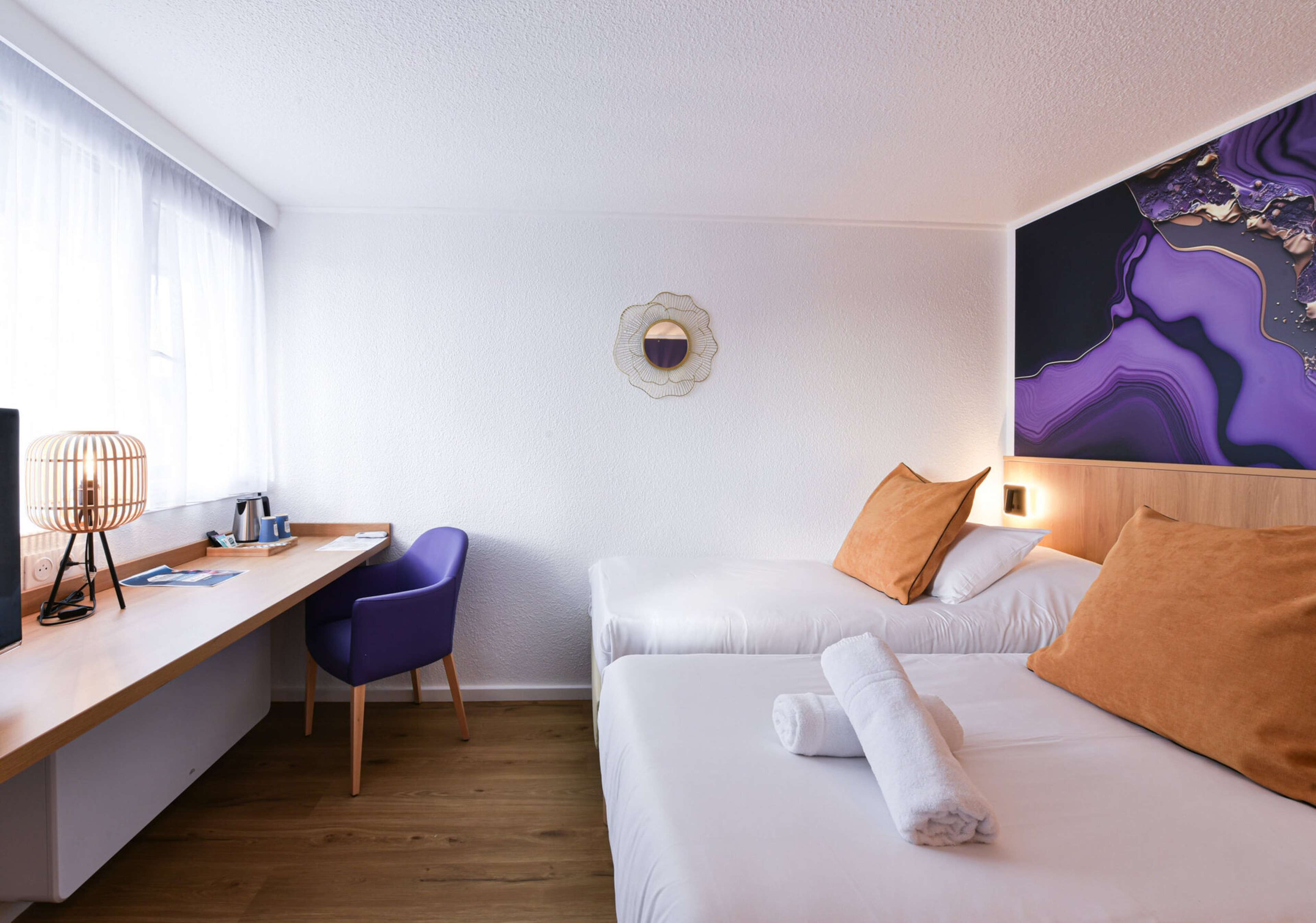 Una habitación de hotel con escritorio, dos camas, una silla y una obra de arte en la pared.