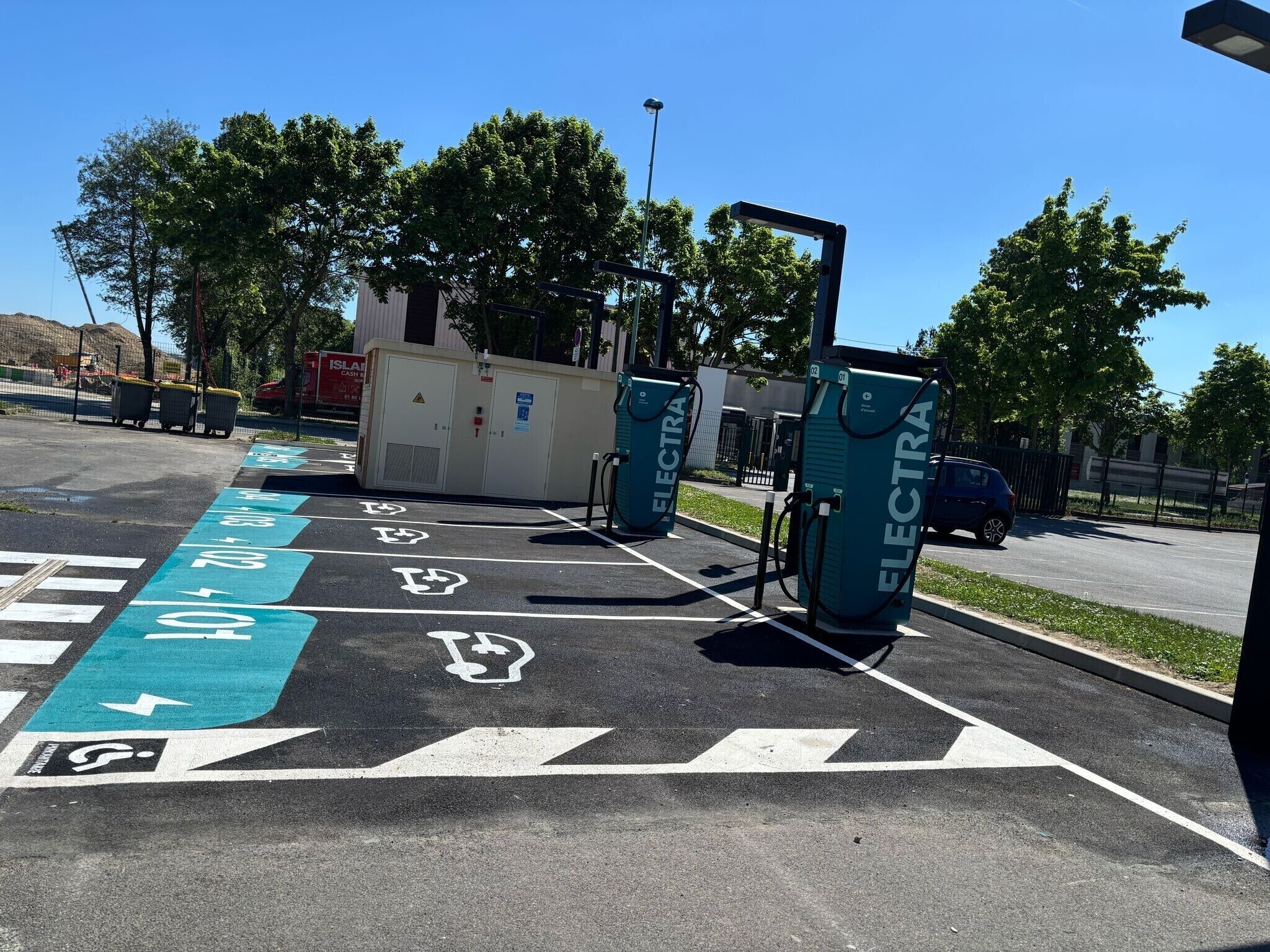 Une zone équipée de bornes de recharge pour véhicules électriques, avec des places de stationnement réservées et un bâtiment en arrière-plan.