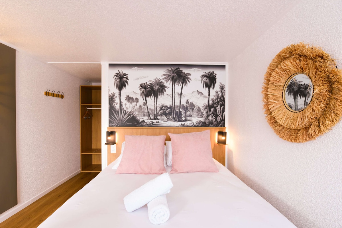 A hotel room with a bed, a headboard with a tropical mural, a round mirror, and a wooden wardrobe.