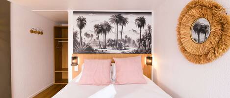 A hotel room with a bed, a headboard with a tropical mural, a round mirror, and a wooden wardrobe.