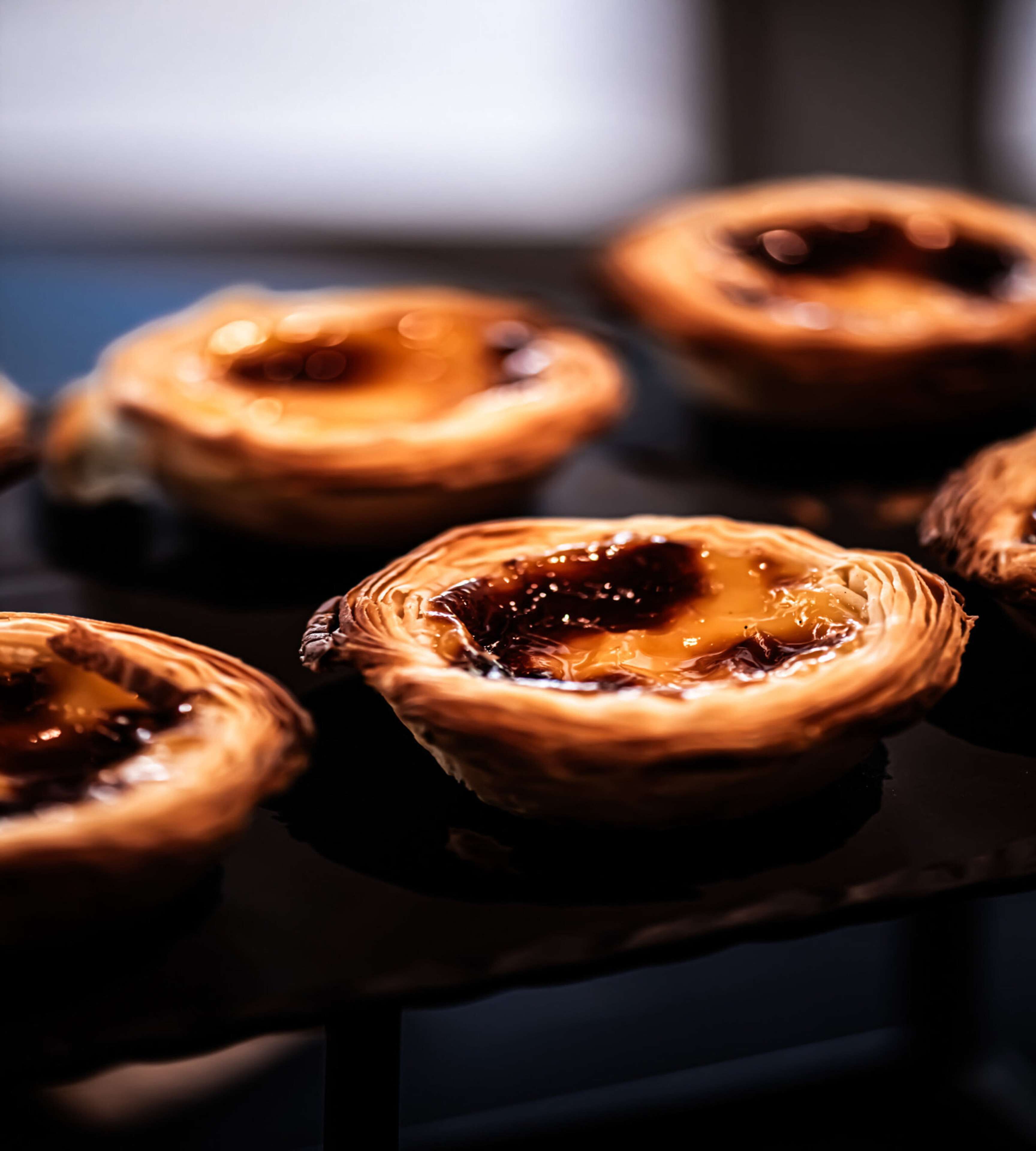 A close-up of several Portuguese egg tarts with caramel on a dark surface.