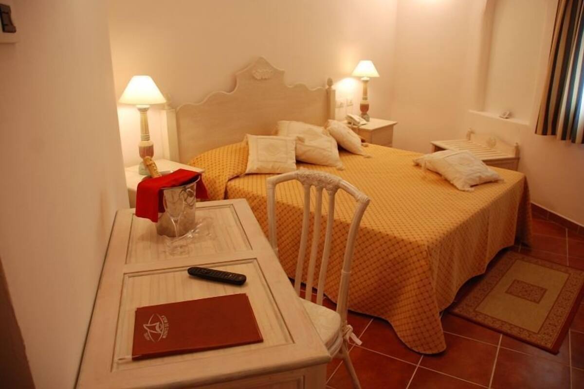 Une chambre d’hôtel avec un lit, des tables de chevet, une chaise, un bureau avec une télécommande et un dossier rouge.