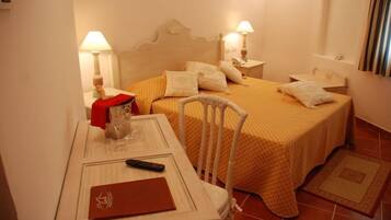 Habitación de hotel con cama, mesitas de noche, una silla, un escritorio y un archivador rojo.