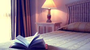 Un lit bien fait, avec un livre ouvert posé dessus, une lampe de chevet et une petite table à côté du lit.