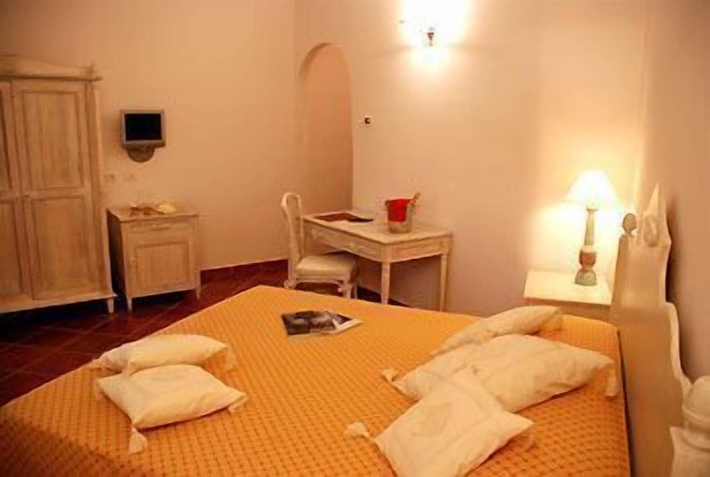 Quarto de hotel com cama, escrivaninha, cadeira, mesa de cabeceira e abajur.