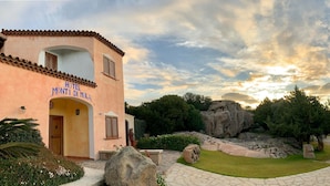 Un hôtel à la façade rose, doté d’un chemin bordé de pierres et entouré de verdure.