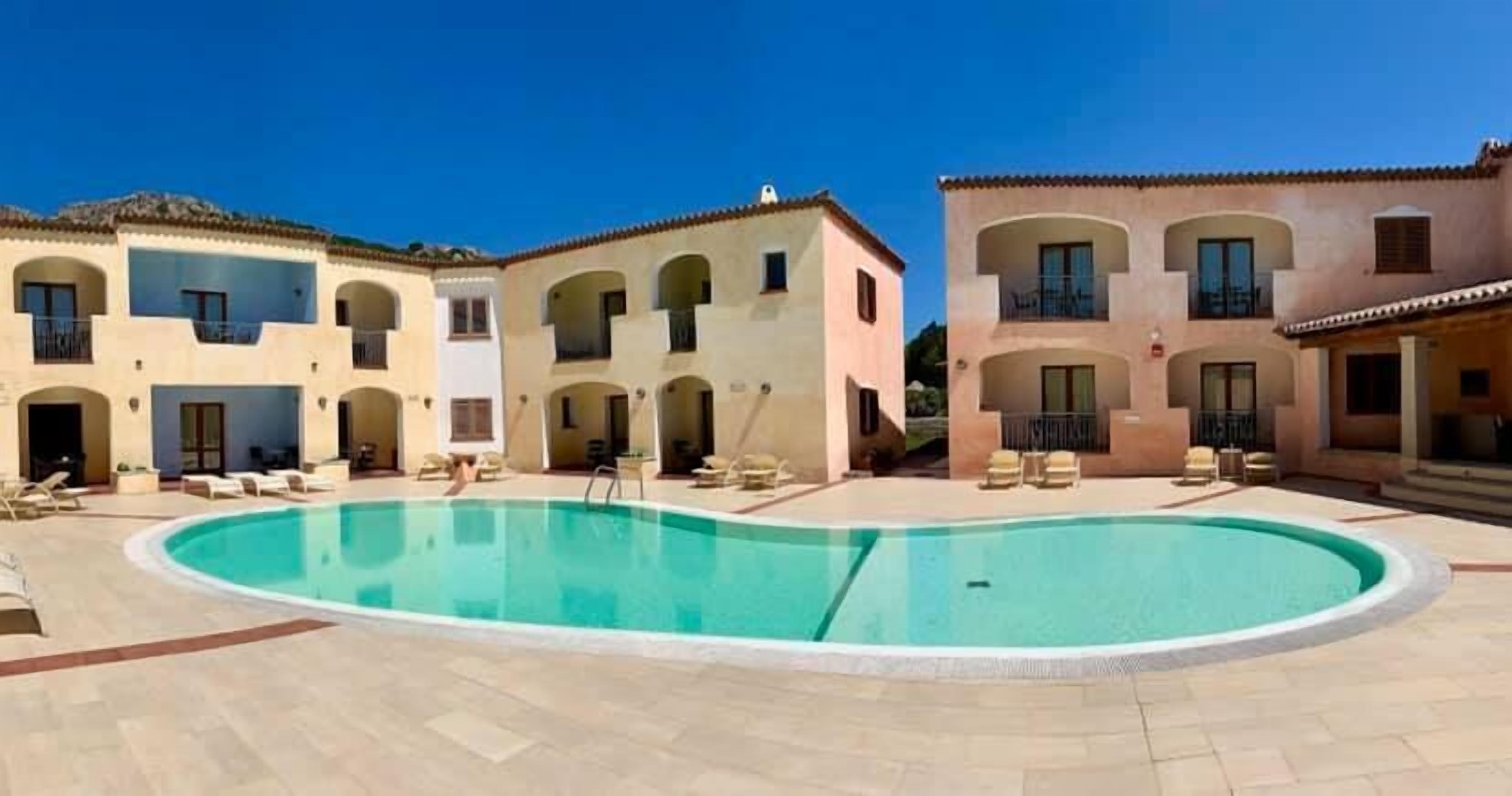 A hotel with a central swimming pool surrounded by multiple buildings with balconies and outdoor seating areas.