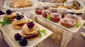 Ein Buffet mit verschiedenen Backwaren und Desserts, darunter Pfannkuchen mit Kirschen, Muffins und eine Kuchenplatte.