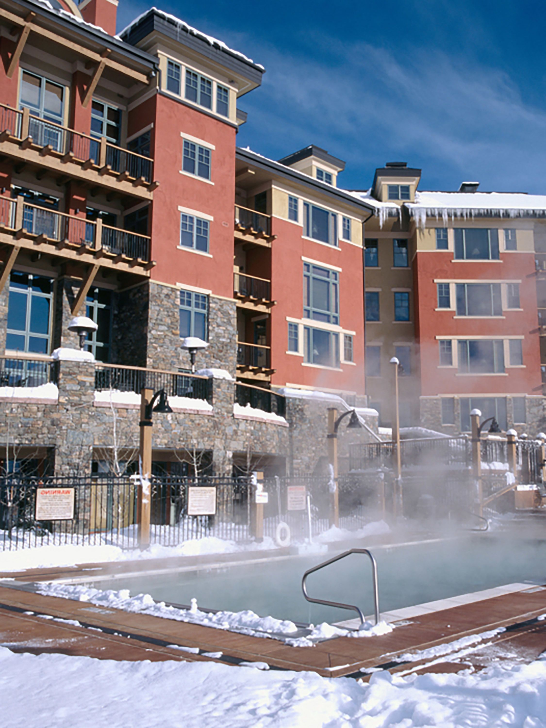 A multi-story hotel with balconies, a pool area with a hot tub, and a stone facade.