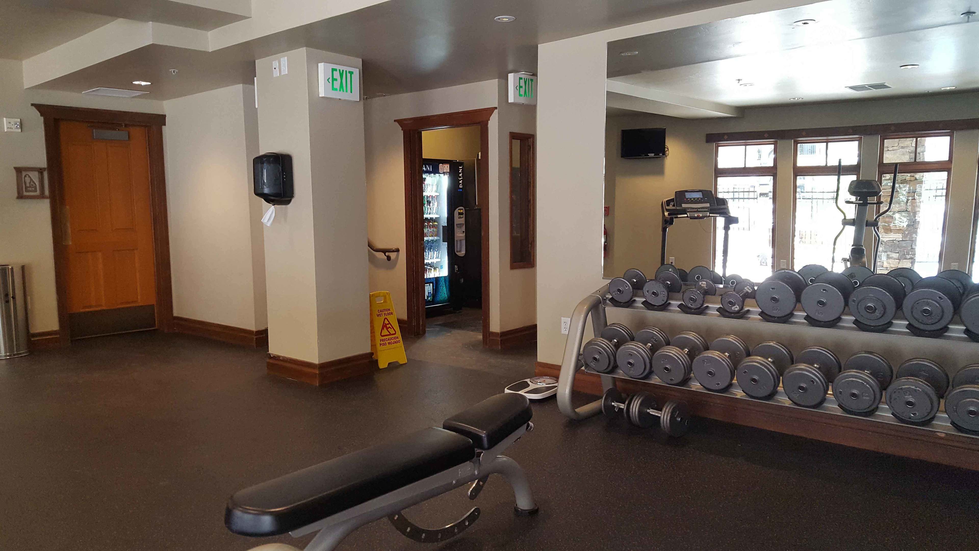 Un gimnasio con una banca, un estante de mancuernas y una señal de salida.