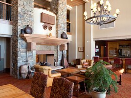 A spacious lobby with a stone fireplace, leather seating, a large chandelier, and a bar area.