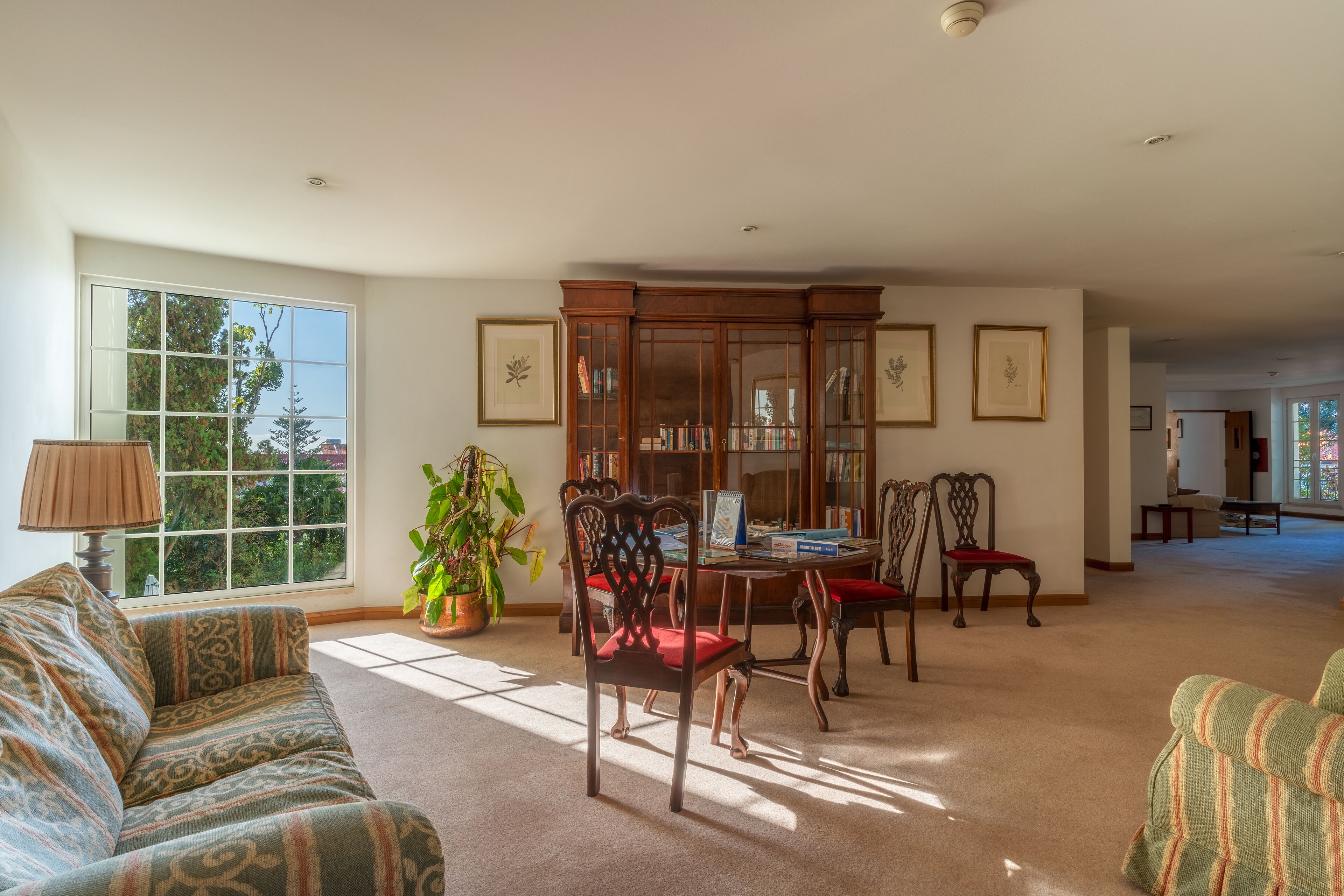 A spacious living room with a large window, a dining area with a wooden cabinet, and a sofa.