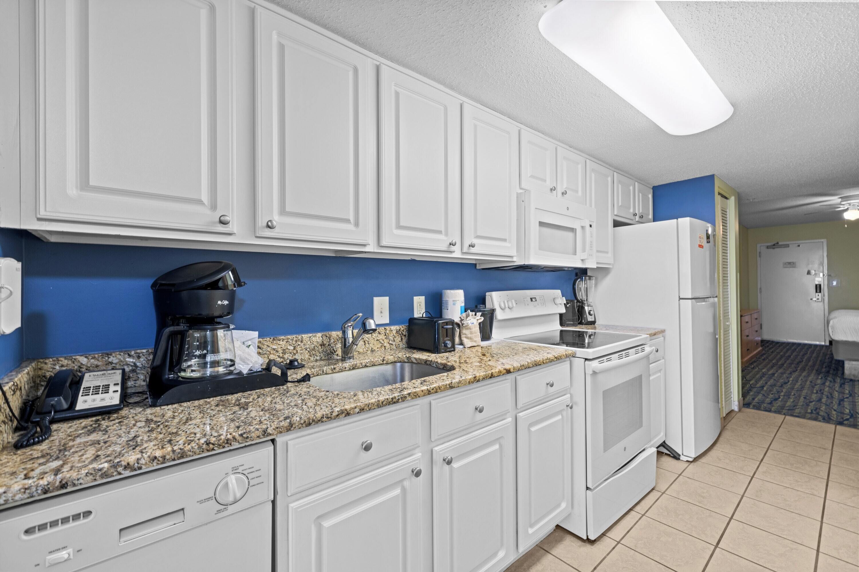 A kitchen with white cabinets, a granite countertop, a coffee maker, a toaster, and a refrigerator.