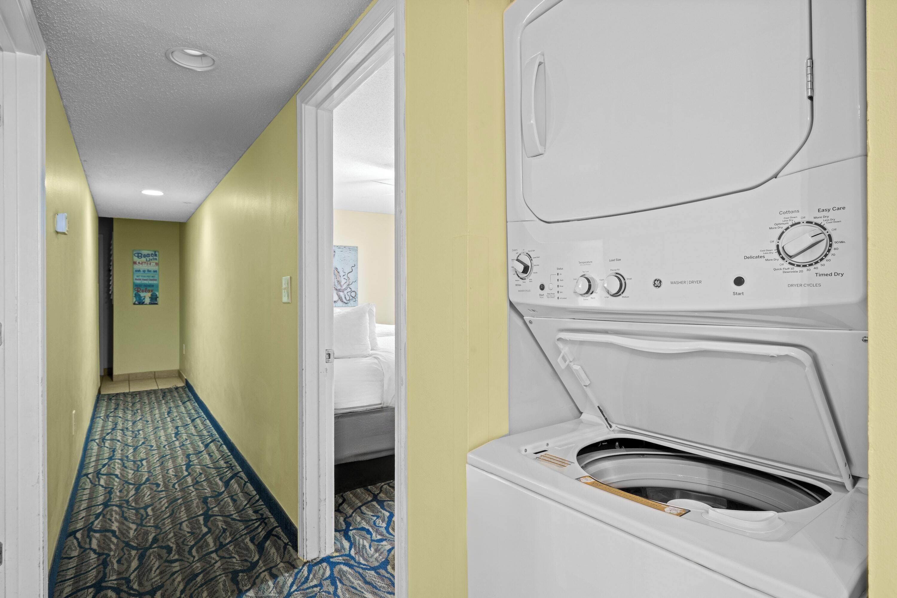 Een hotelgang met een kamer, een vloerkleed met dessin en een wasmachine.
