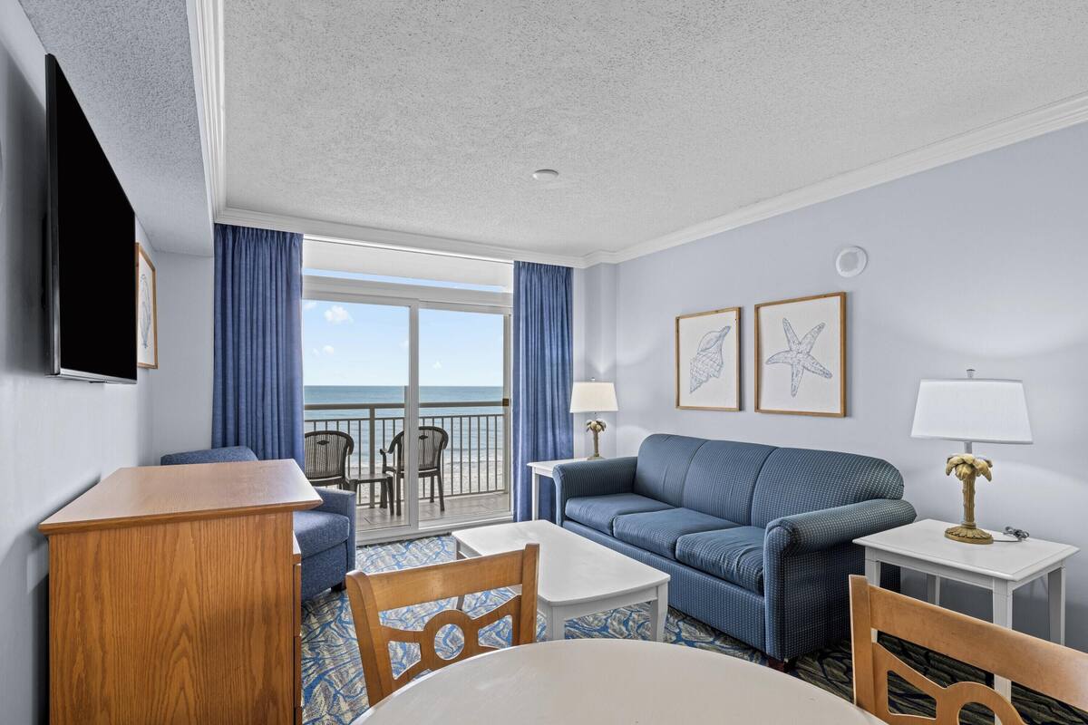 A hotel room with a balcony, a sofa, a table, and a TV.