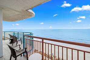 A balcony with chairs and a table overlooking the ocean.