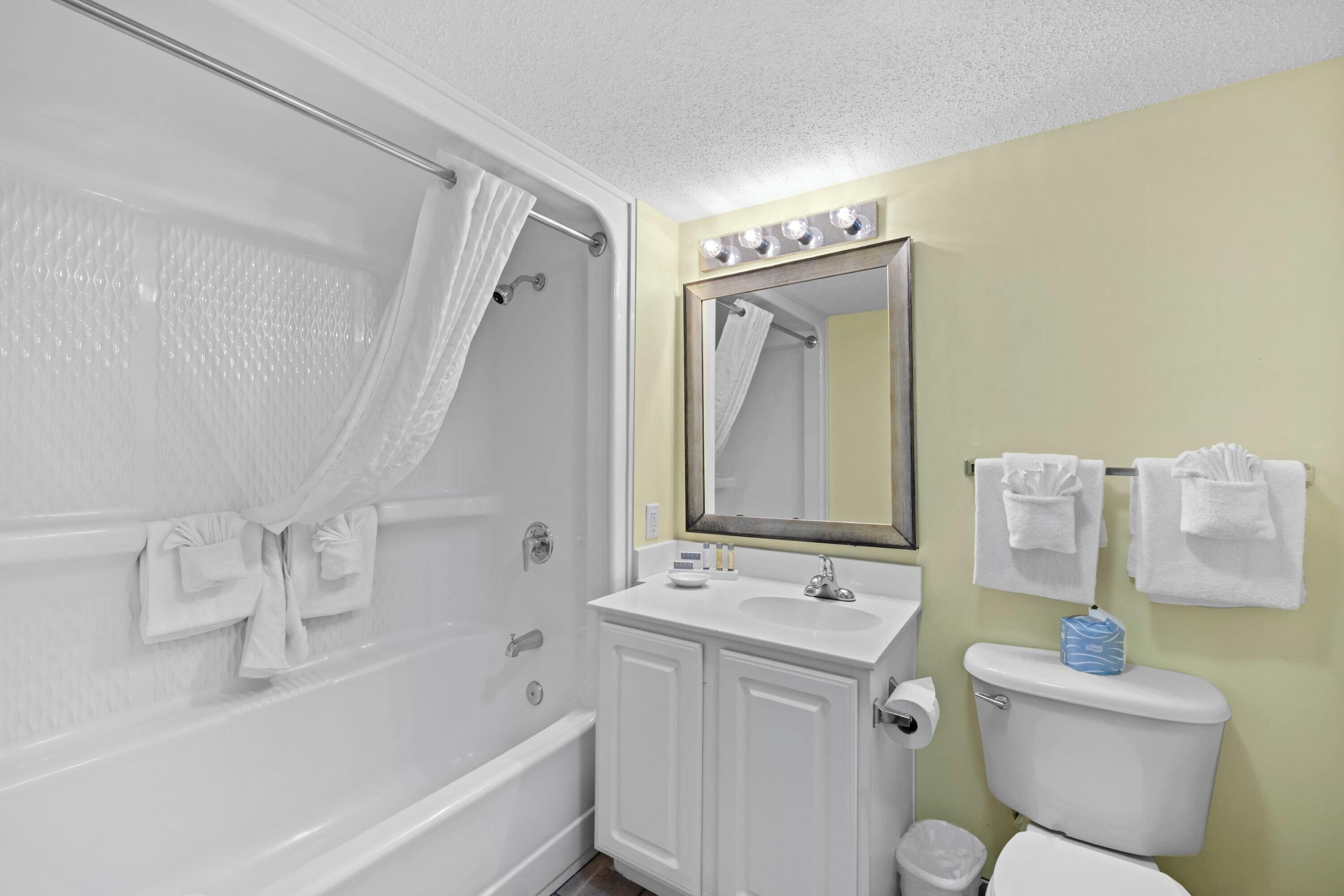 A bathroom with a bathtub, a sink, a toilet, and a mirror with lights above it.