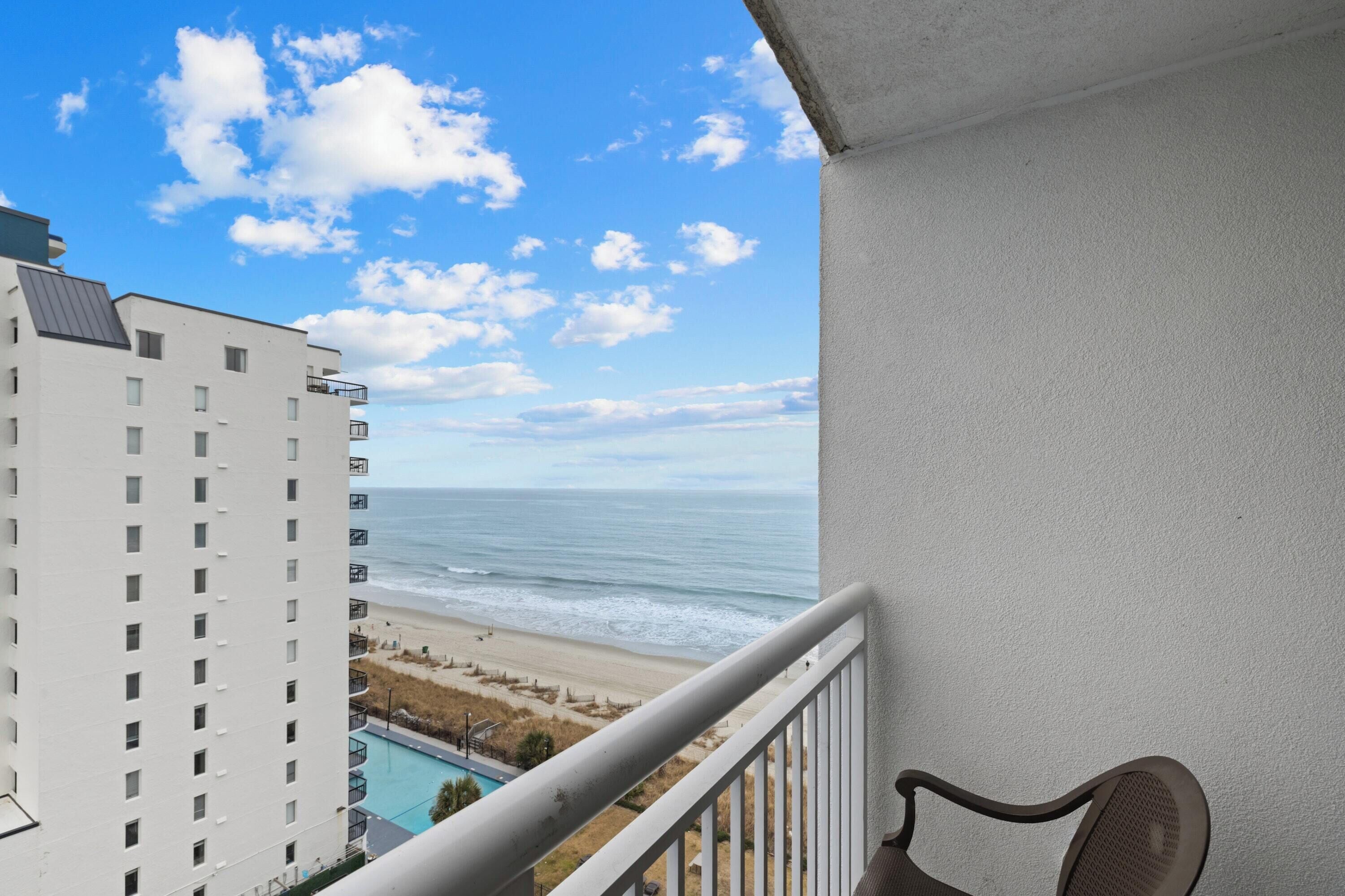 Un balcon avec vue sur la plage et l’océan, une chaise et une piscine.