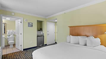 A hotel room with a large bed, a wooden headboard, a microwave, a refrigerator, and a bathroom with a toilet and sink.