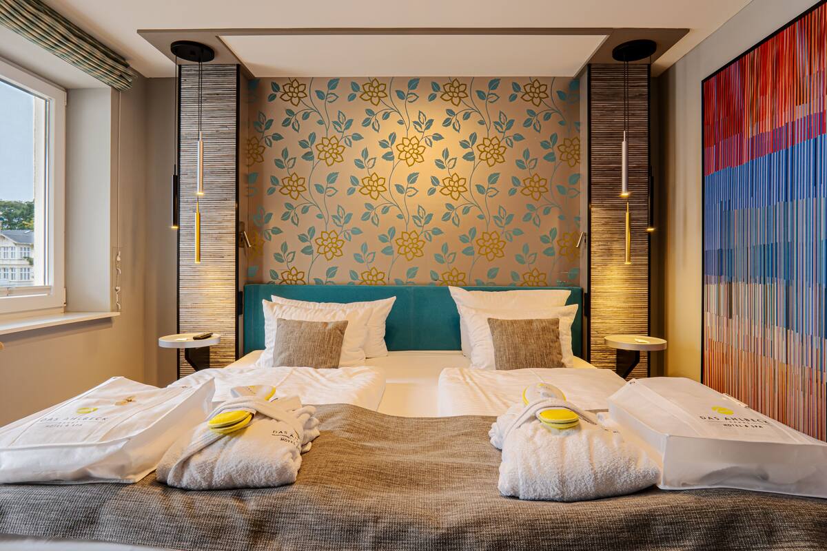 Une chambre d’hôtel avec un grand lit, deux tables de chevet, une fenêtre et un mur décoratif orné d’un motif floral.