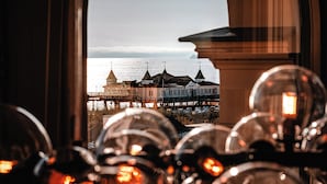 A view through a window with a reflection of a building with multiple spires, a body of water, and a bridge in the background.