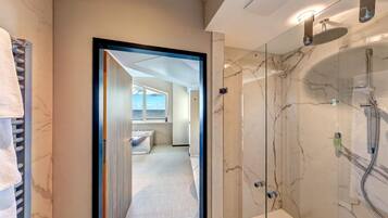 A modern bathroom with a glass-enclosed shower, marble walls, and a view of the sea through an open door.