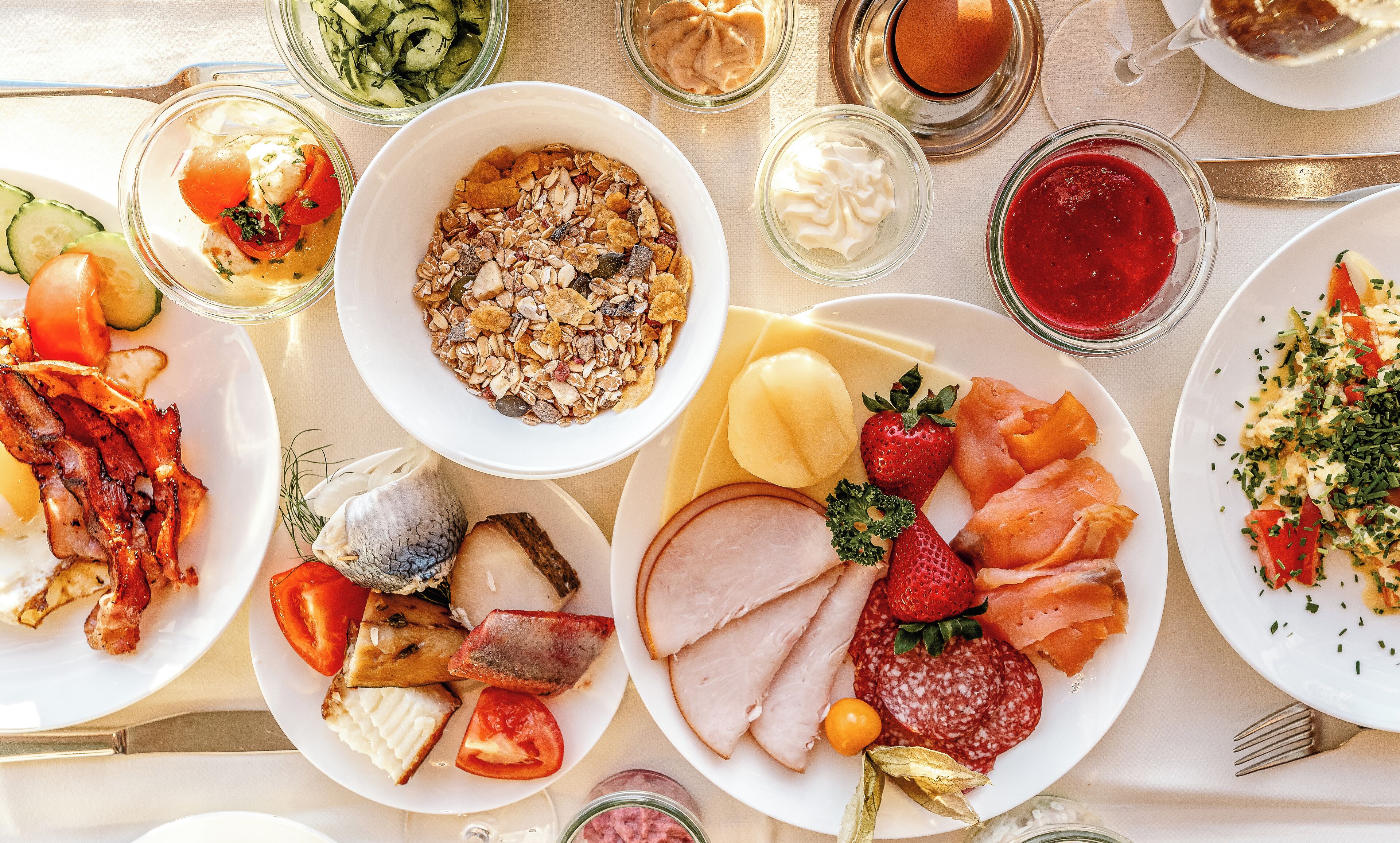 Ein Tisch mit verschiedenen Speisen, darunter Fleisch, Käse, Obst und einer Schüssel Müsli.