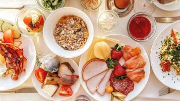 Ein Tisch mit verschiedenen Speisen, darunter Fleisch, Käse, Obst und einer Schüssel Müsli.