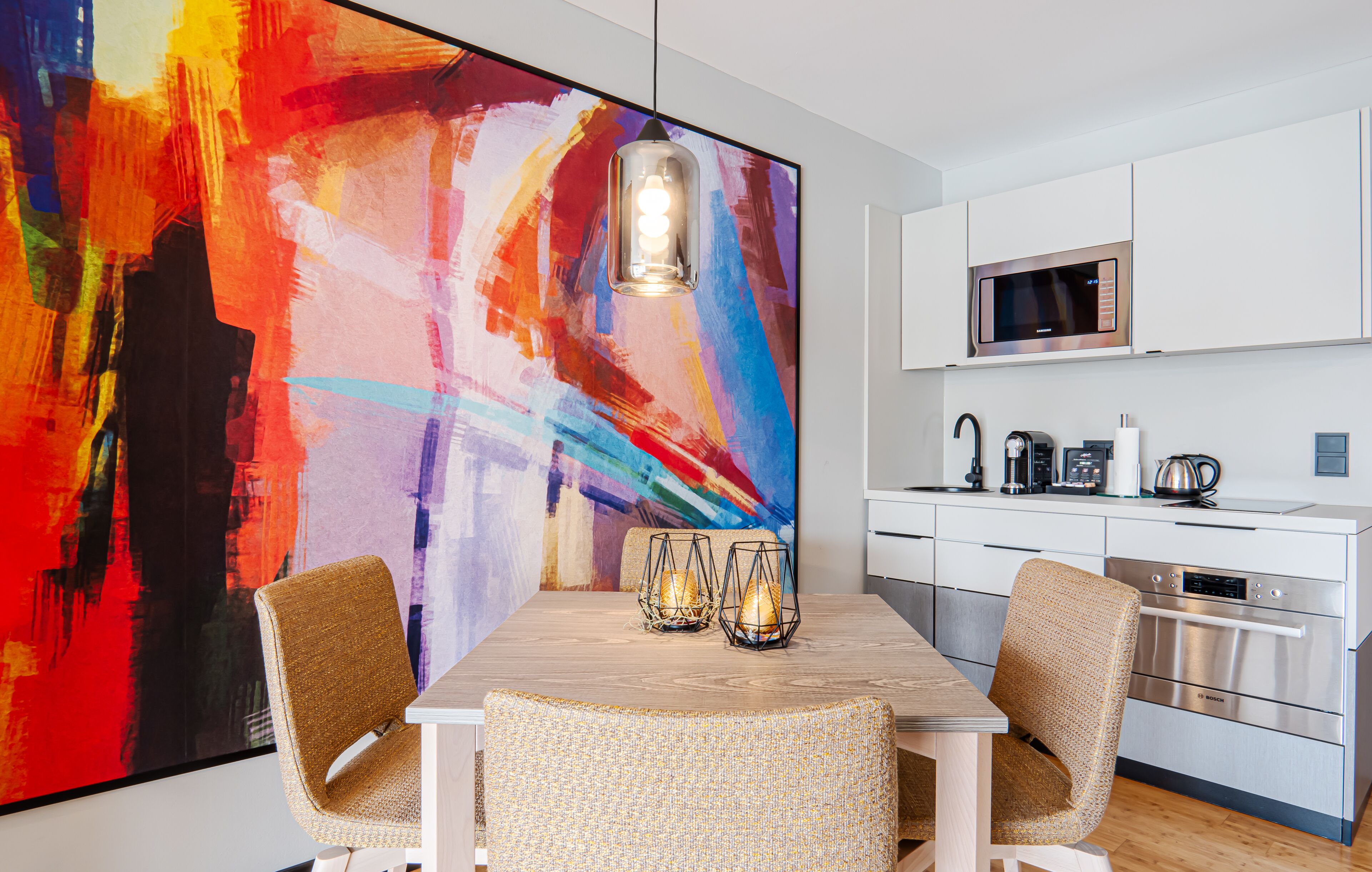 A modern kitchen with white cabinets, stainless steel appliances, and a large abstract painting on the wall.