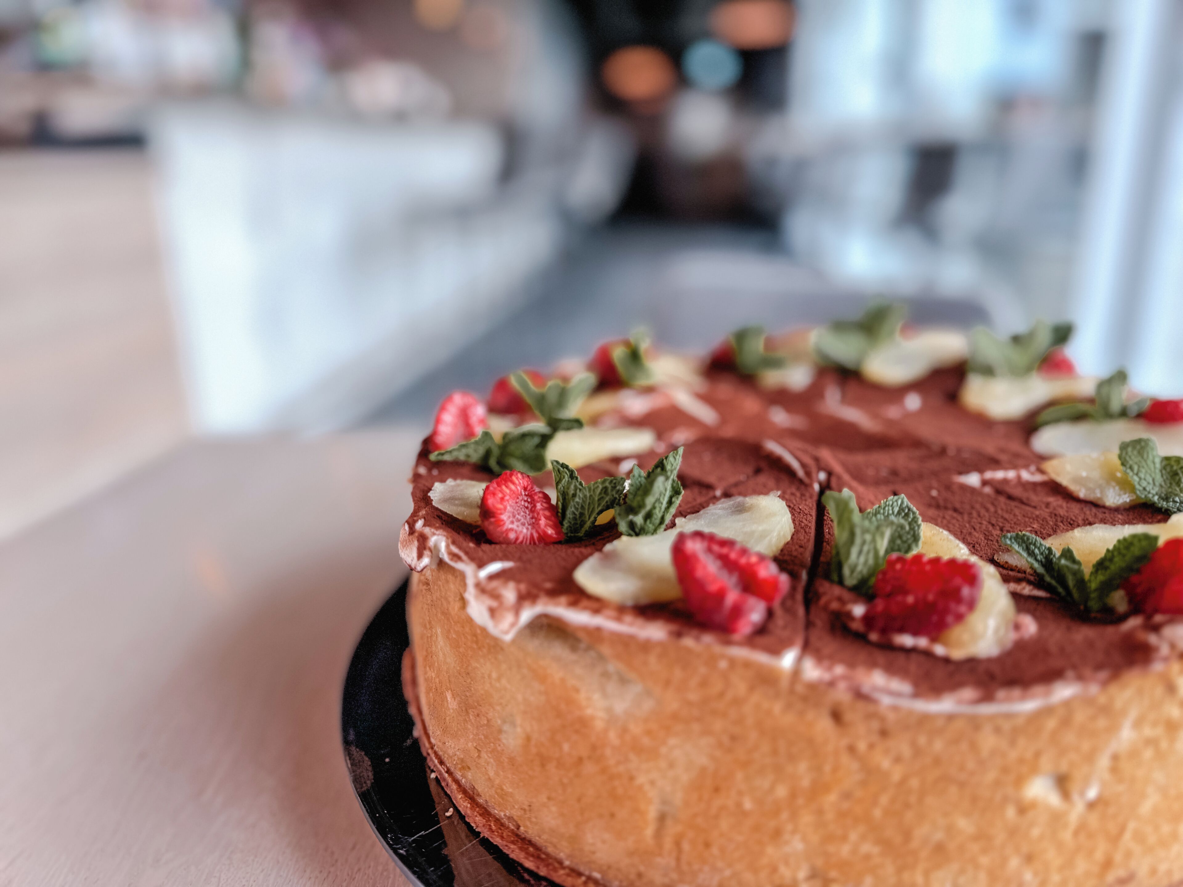 Un gâteau au chocolat, décoré de fraises et de feuilles de menthe, présenté sur une assiette noire.